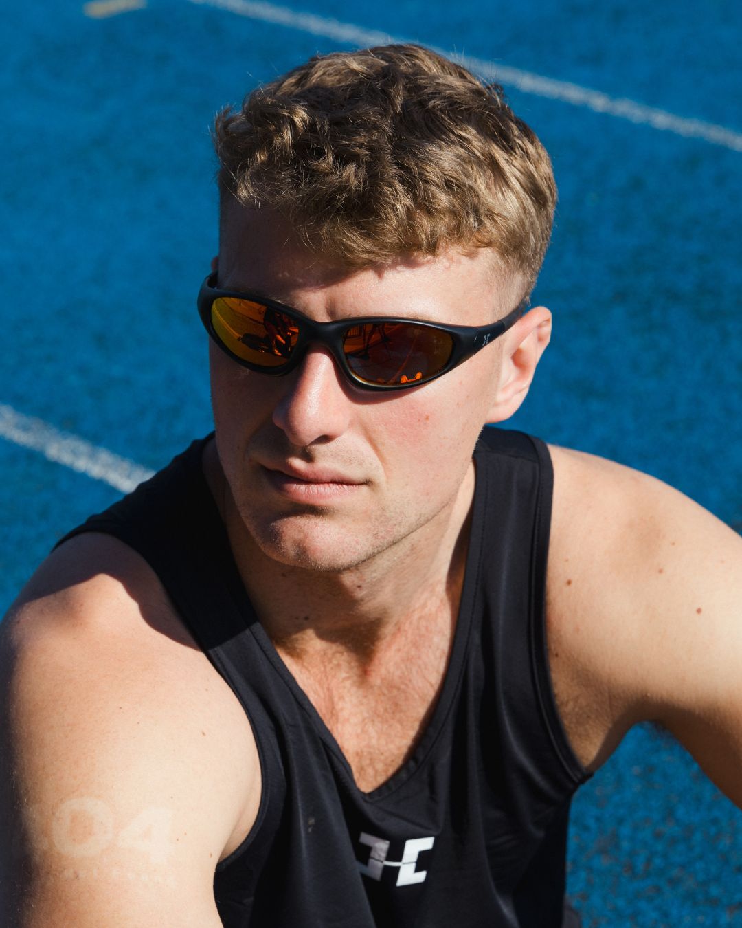 Man wearing sunglasses and a black tank top on a blue track background